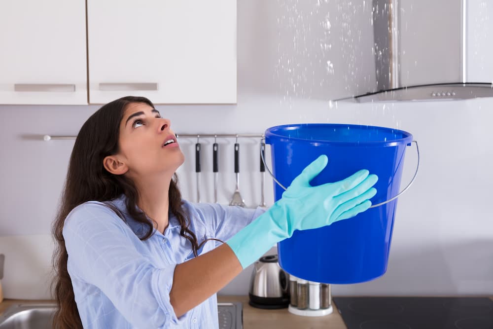 Young woman holding bucket under a roof leak